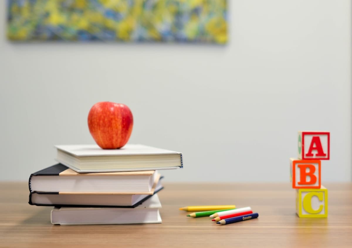 Stack of books, red apple, ABC blocks, and colored pencils on a light wood table