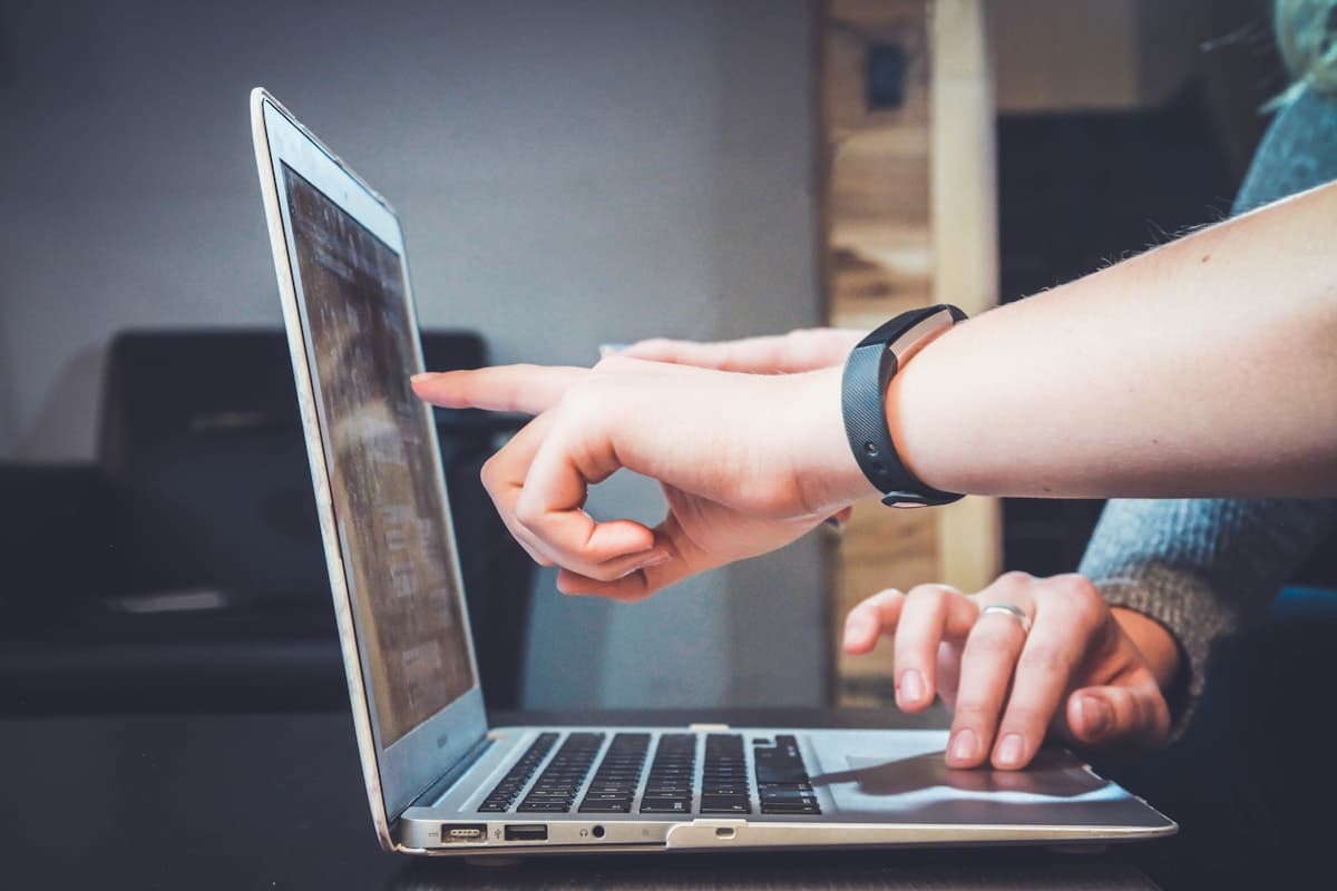Close-up of hands on a silver laptop, one finger pointing at the screen and one hand on the trackpad