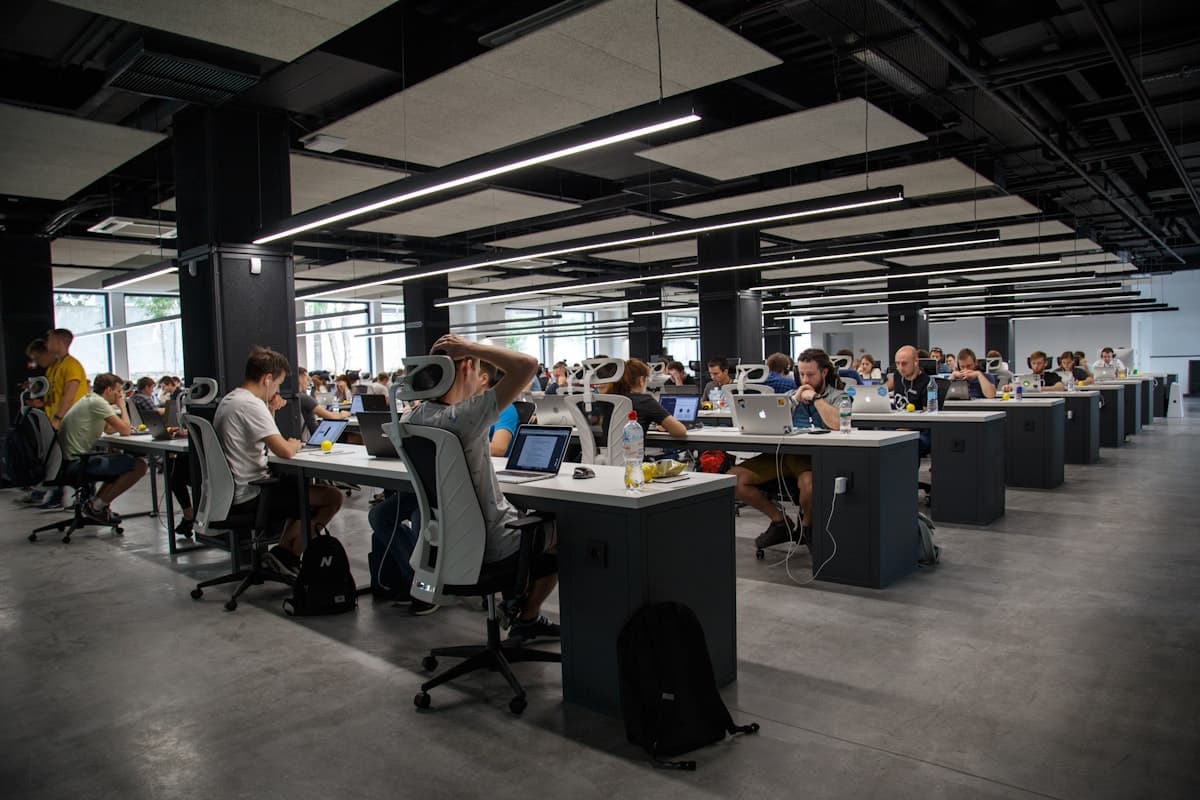 Wide view of a bright co-working space with many people working on laptops at long white desks