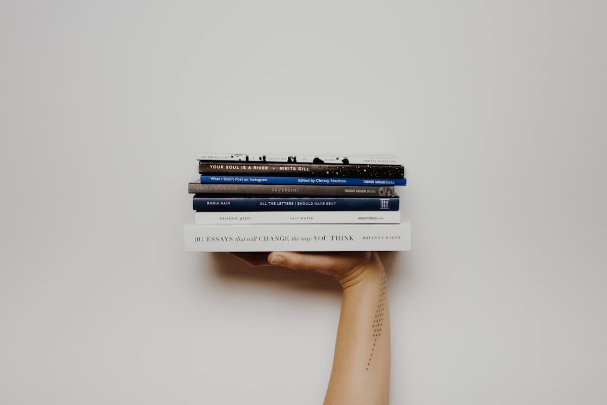 Arm and hand holding a careful stack of books against a simple light background